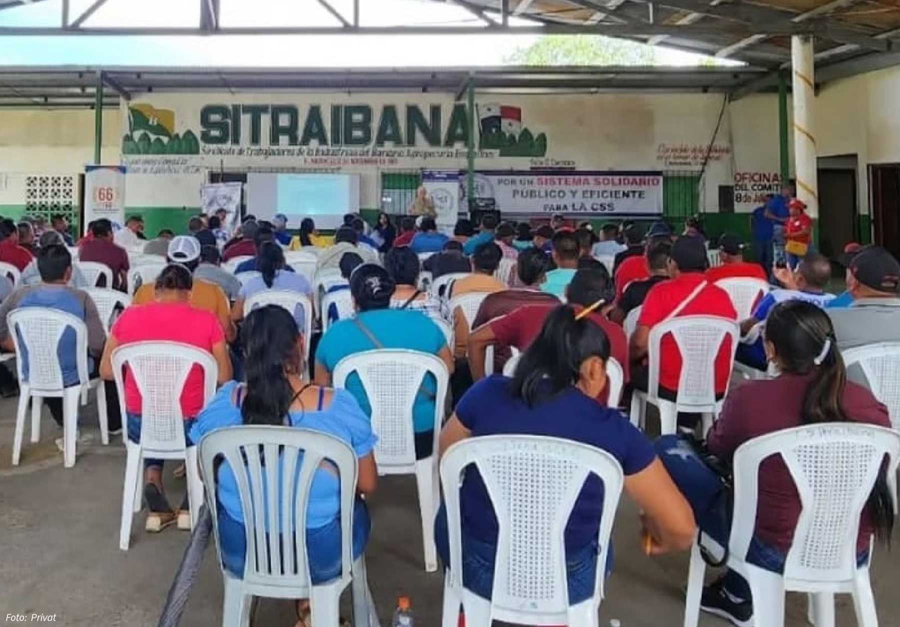 Ein großer Raum mit sitzenden Personen, die sich versammelt haben. An der Rückwand des Raumes ein Transparent mit der Aufschrift "SITRAIBANA". Unterhalb des Banners eine Leinwand und eine Person am Mikro, die augenscheinlich zu den sitzenden Versammelten spricht. Im Bild rechts unter dem Banner ein kleineres mit der Aufschrift "Por un Sistema Solidario Público y Eficiente, LA CSS"