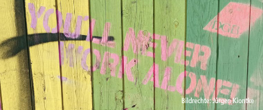 Bunte Holzlatten mit aufgesprühtem Schriftzug ‚You’ll never work alone