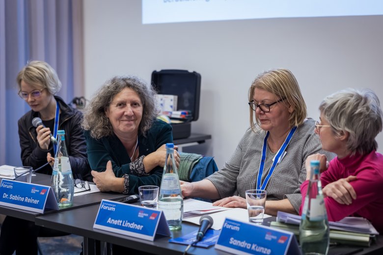 Tagungssituation: 4 Frauen, nebeneinander am Tisch sitzend. Mit Tisch-Namensschildern davor.