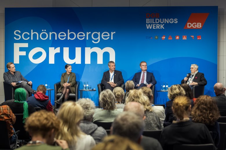 Eine Tagungssituation. 5 Menschen auf einem Podium, nebeneinander sitzend. Im Hintergrund ein große Leinwand mit dem Schriftzug: Schöneberger Forum und den Logos DGB Bildungswerk und DGB sowie weiteren Logos.