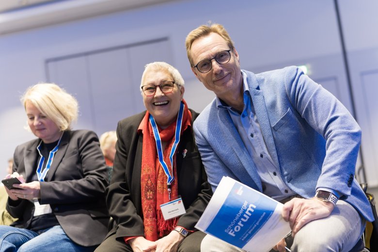 Gruppe reckt die Arme und steht vor einem blauen Rückwand mit dem Schriftzug Schöneberger Forum