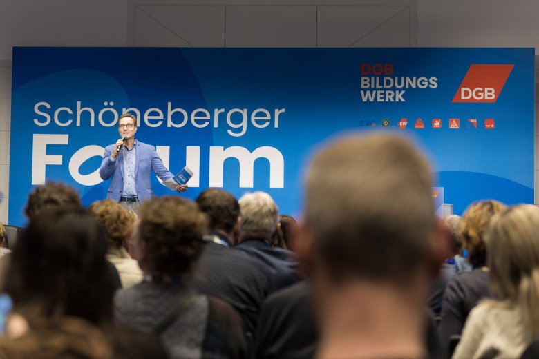 Gruppe reckt die Arme und steht vor einem blauen Rückwand mit dem Schriftzug Schöneberger Forum