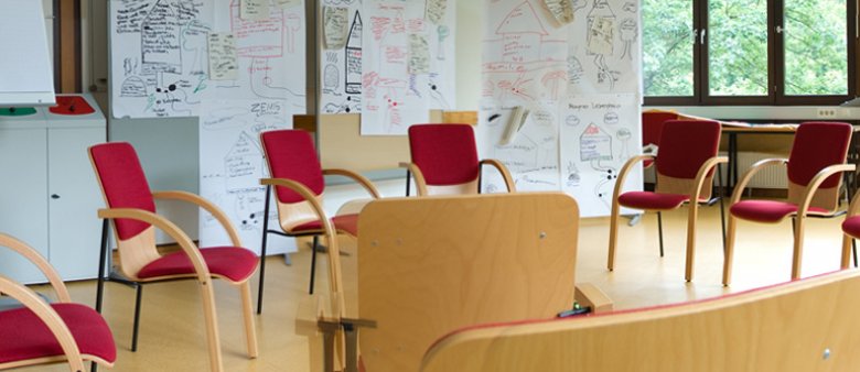 Stuhlkreis in einem Seminarraum, an den Wänden hängen große Papierbögen mit handschriftlichen Notizen und Zeichnungen