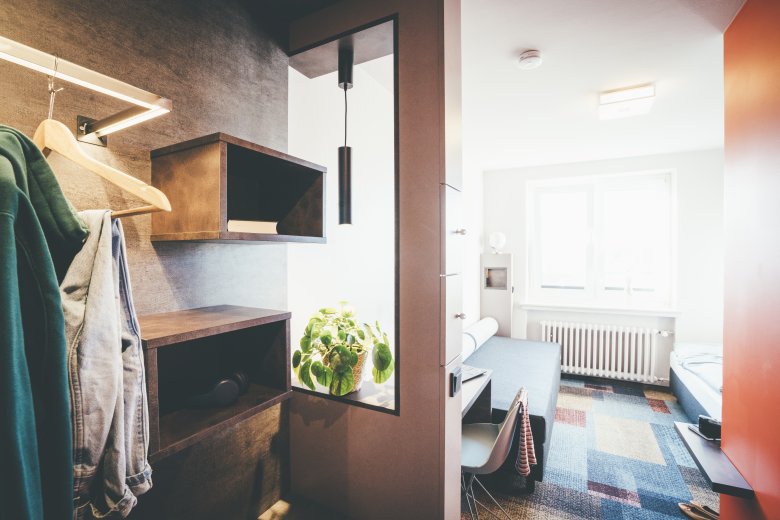 Helles, modern eingerichtetes Gästezimmer mit Schreibtisch, Stuhl, Bett und offener Garderobe