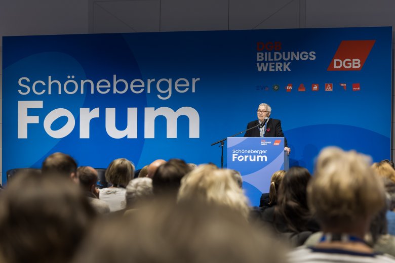 Eine Frau steht am Rednerpult vor eine Leinwand mit dem Schriftzug Schöneberger Forum sowie mit Logos des DGB Bildungswerk, des DGB und weiteren Einzelgewerkschaften. Im Vordergrund Menschen in Stuhlreihen von hinten.