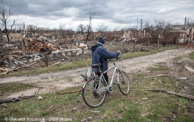 Ein durch den Krieg verwüsteter Landstrich in der Ukraine. Ein Mann schiebt sein Fahrrad durch unwegsames Gelände